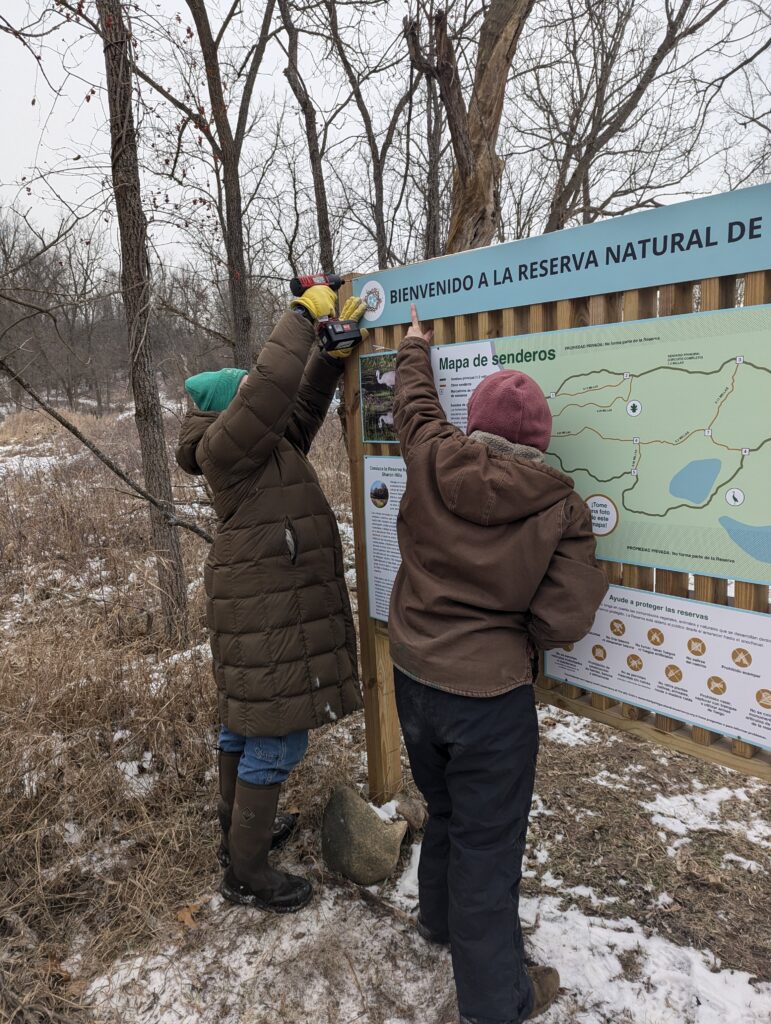 Ari and Kyler screw in a sign on the Sharon Hills Preserve kiosk