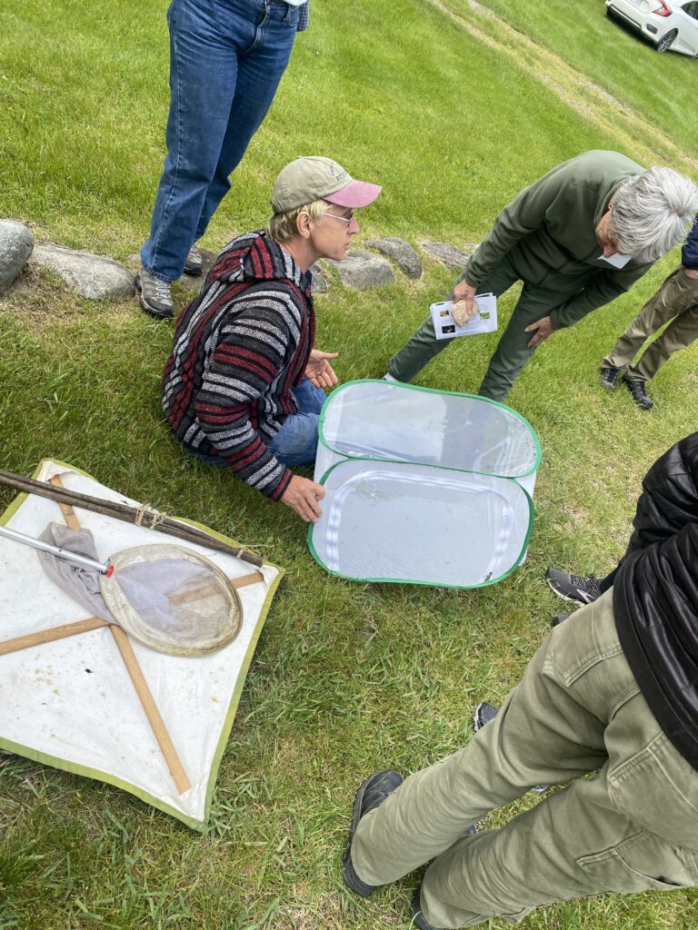 Man sitting on the grass with bug nets talking to a woman