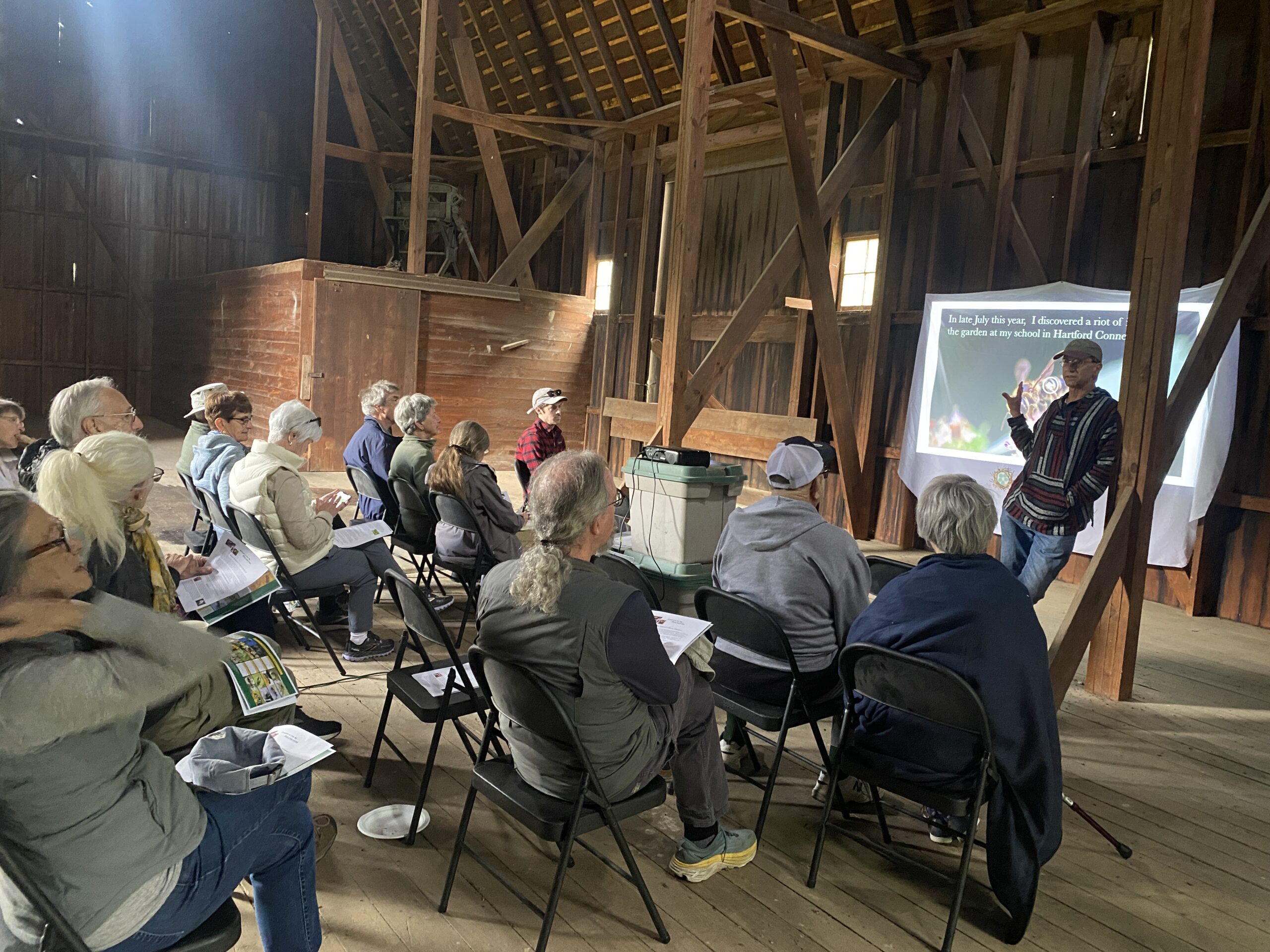 Group of people sitting in a barn listening to a man speak