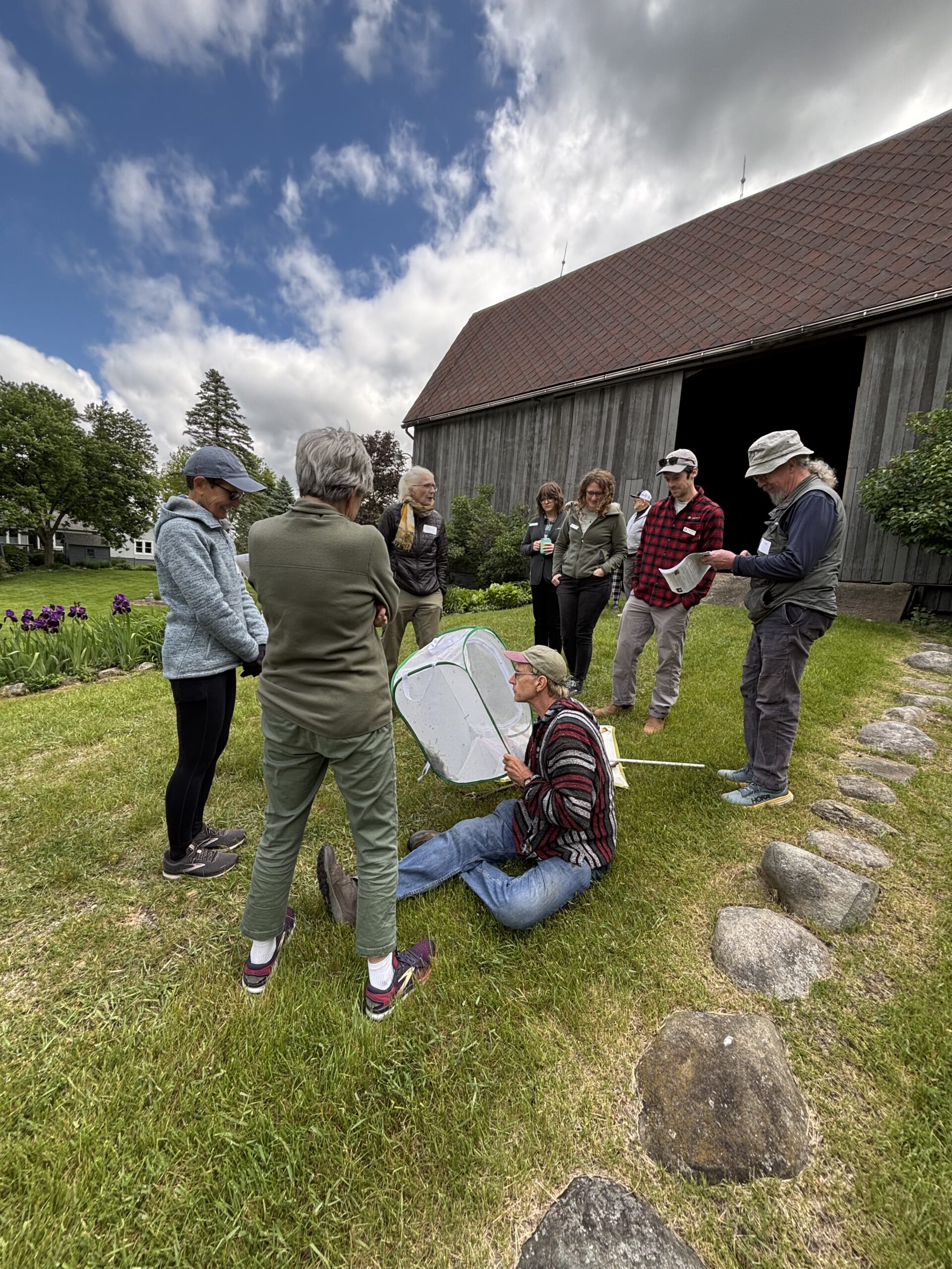 Man sitting on the ground talking to a group of people outside a barn