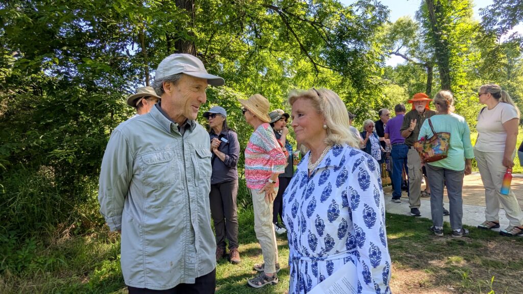 Two people talk and smile. Many other people in the background talk.