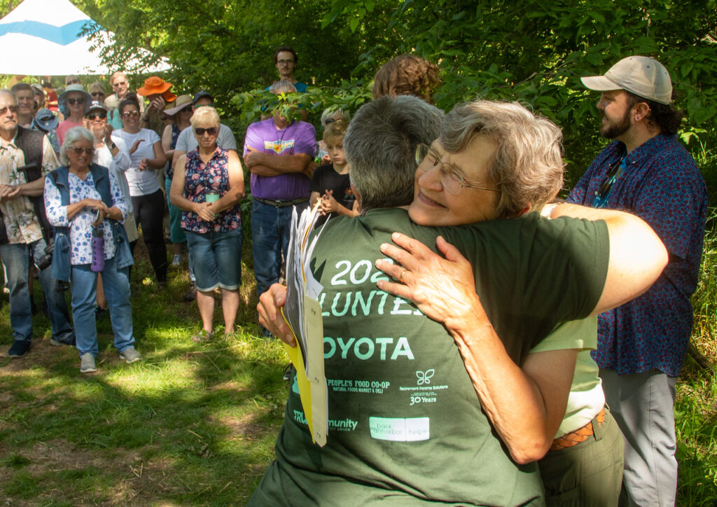 Two people hug. Many people stand in the background watching.
