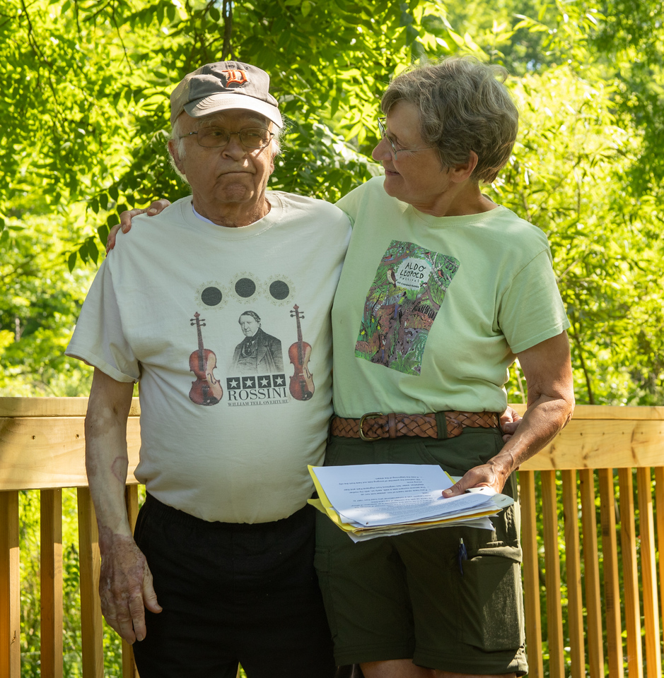 Two people smiling and standing on a wooden bridge.