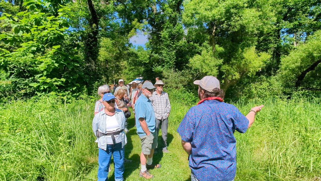 A group of ten people stand on a green trail with green plants and trees.