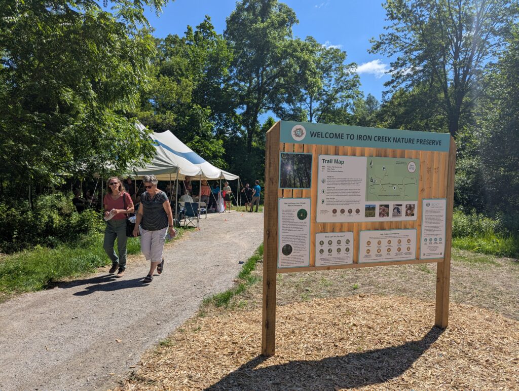Two people walk by the Welcome to Iron Creek Preserve kiosk