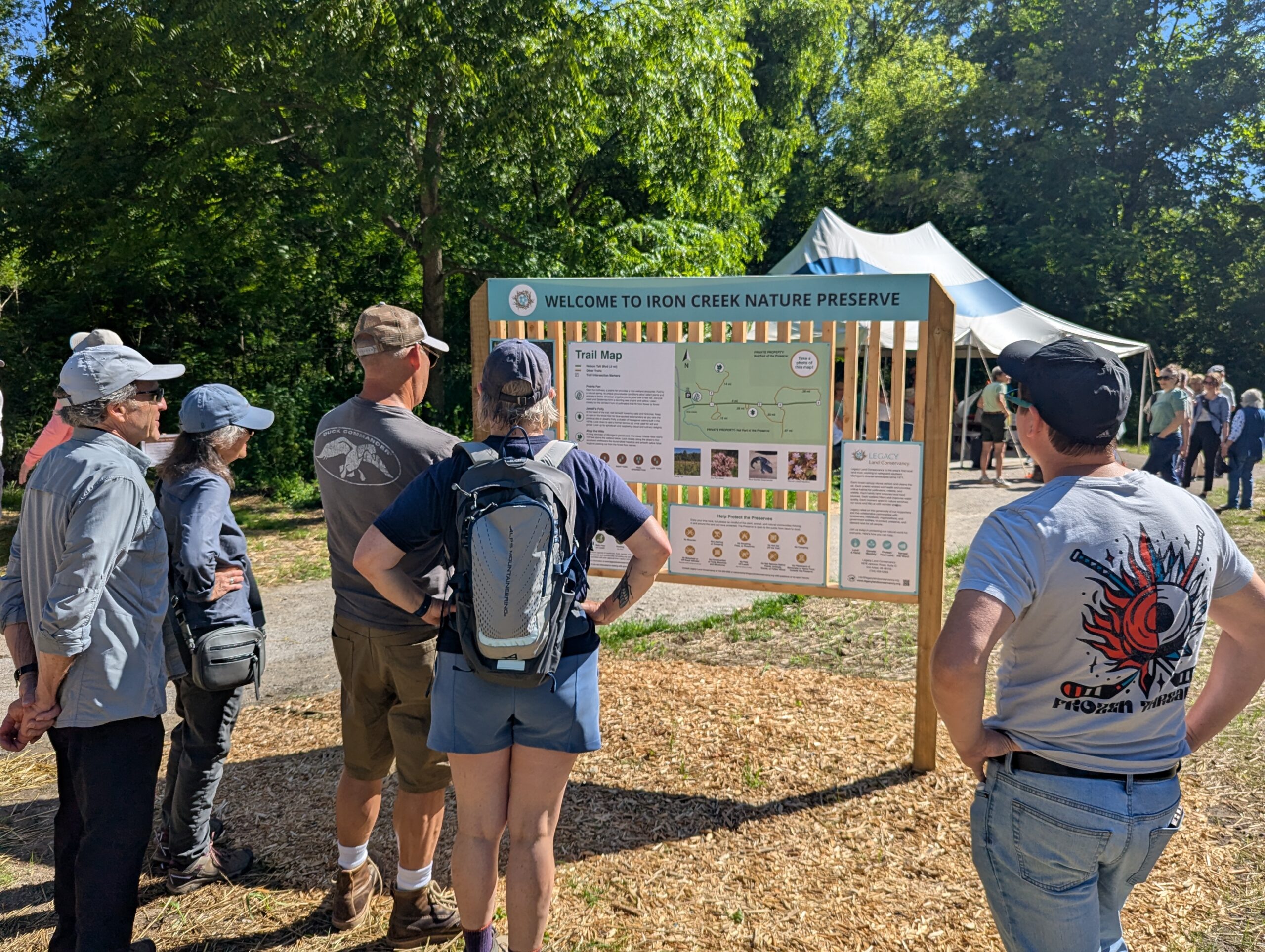 Six people stand and read the signs on a Welcome to Iron Creek Preserve wooden kiosk.