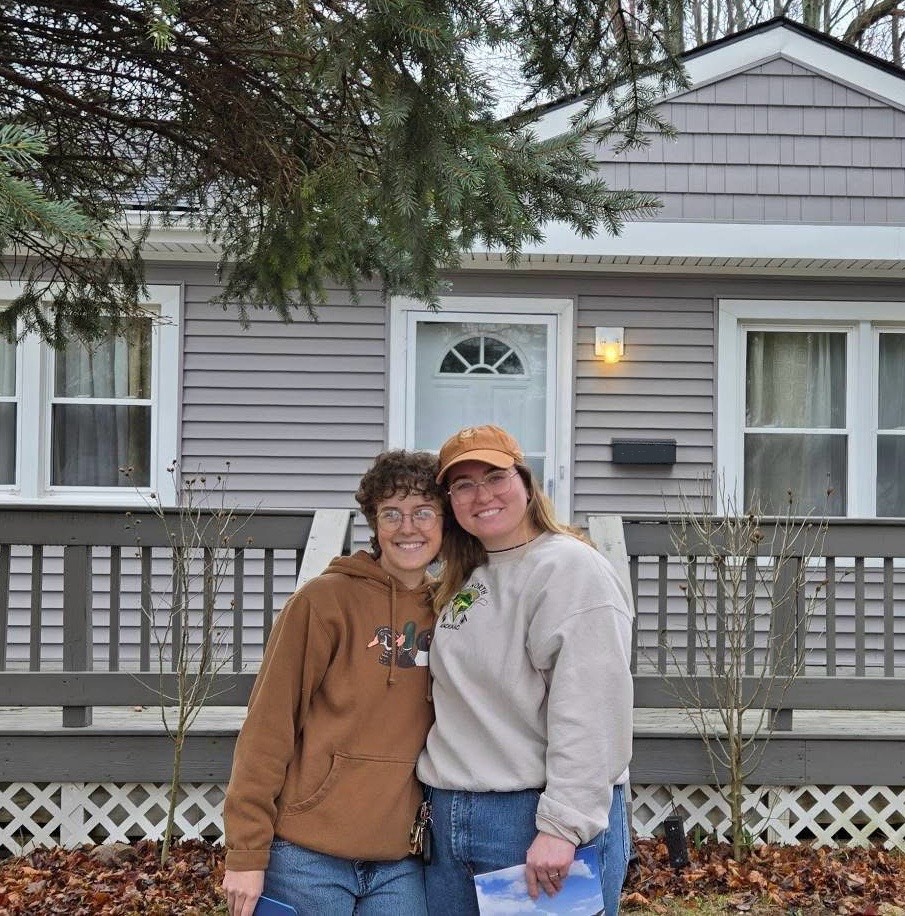 Two people embracing in front of a house.