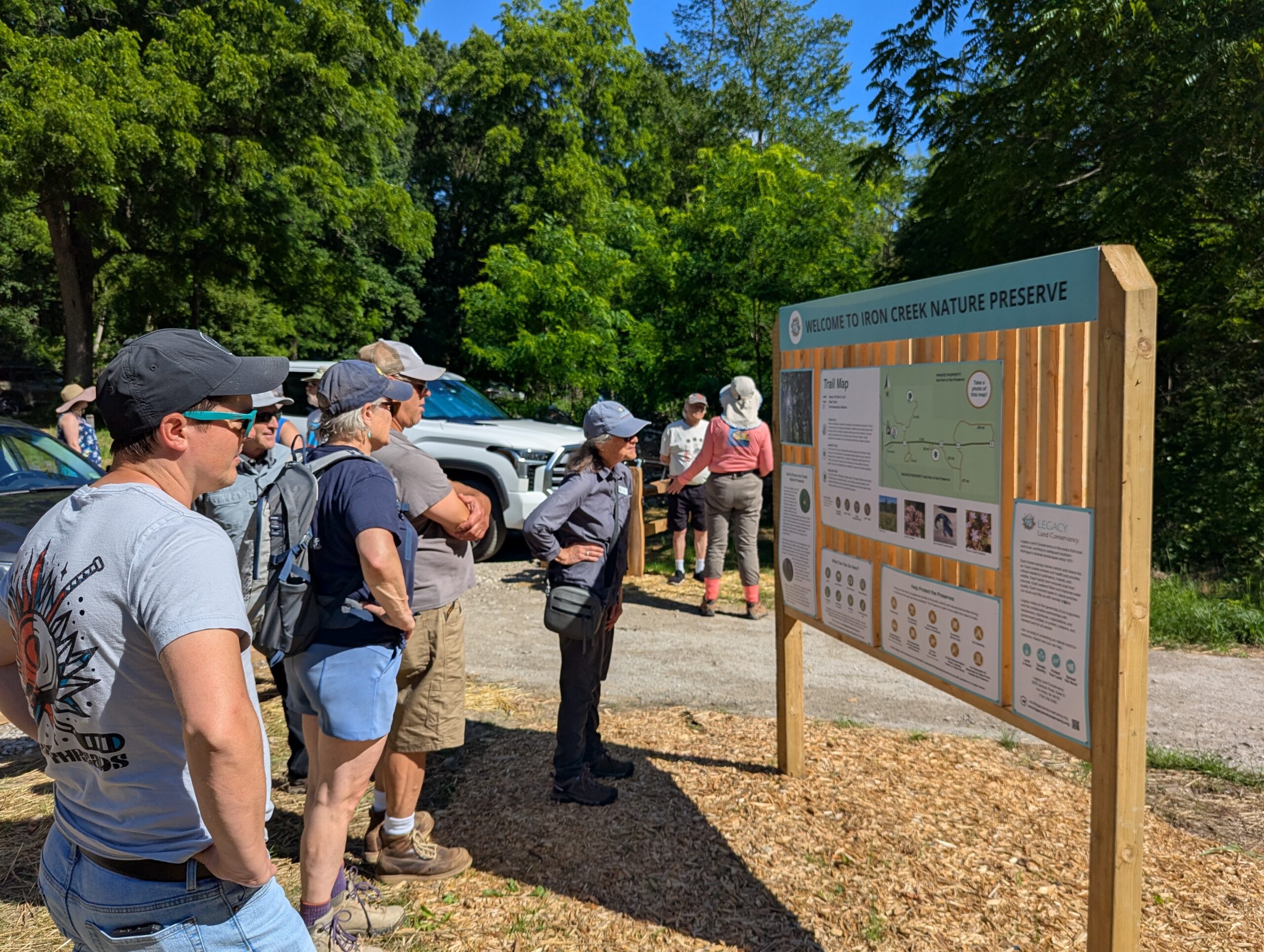 Group of people stand in front of a wooden kiosk with nature preserve informational signs.